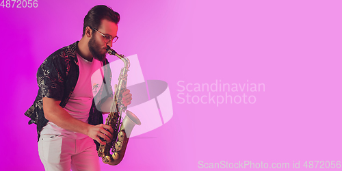 Image of Young caucasian jazz musician playing the saxophone in neon light, flyer with copyspace for ad