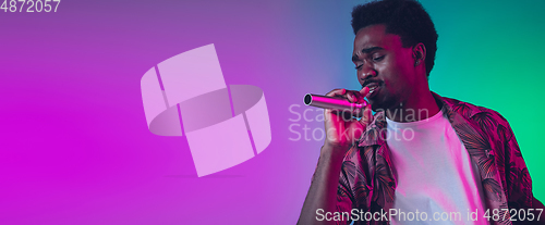 Image of African-american male singer portrait isolated on gradient studio background in neon light, flyer with copyspace