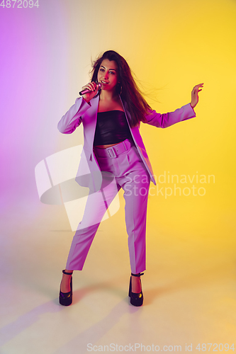 Image of Caucasian female singer portrait isolated on gradient studio background in neon light