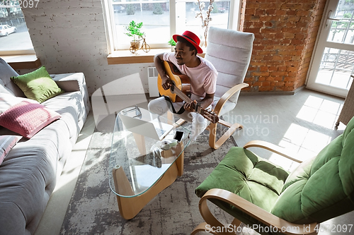 Image of African-american musician playing guitar during online concert at home isolated and quarantined, impressive improvising