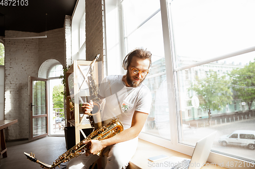 Image of Caucasian musician choosing instrument for concert at home isolated and quarantined, impressive improvising with band connected online