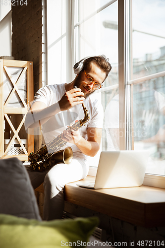 Image of Caucasian musician playing saxophone during online concert at home isolated and quarantined, impressive improvising