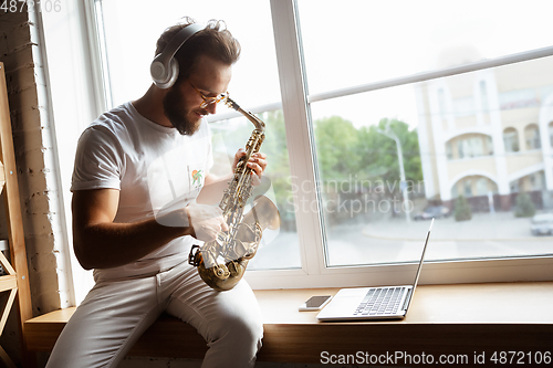 Image of Caucasian musician playing saxophone during online concert at home isolated and quarantined, impressive improvising