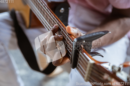 Image of Close up of african-american musician playing guitar during online concert at home isolated and quarantined, impressive improvising