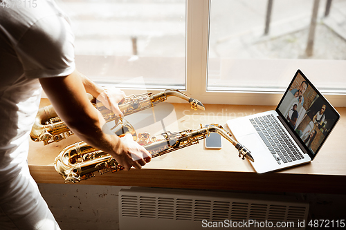 Image of Caucasian musician playing saxophone during concert at home isolated and quarantined, impressive improvising with band connected online