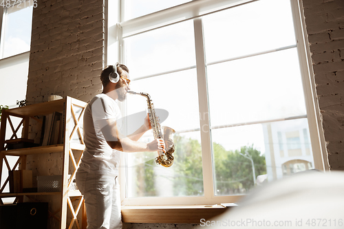 Image of Caucasian musician playing saxophone during online concert at home isolated and quarantined, impressive improvising