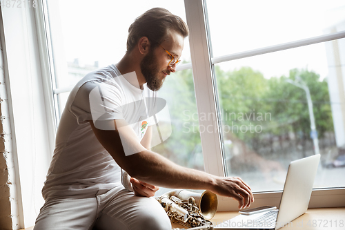 Image of Caucasian musician preparing for concert at home isolated and quarantined, impressive improvising with band connected online