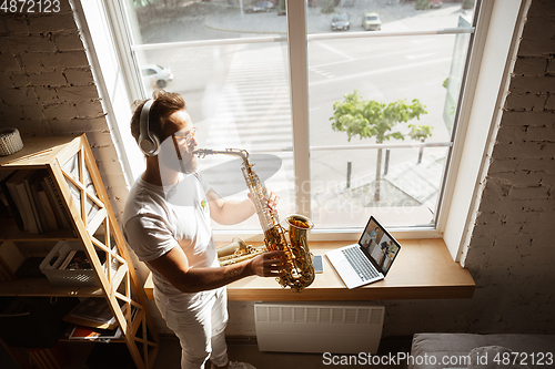 Image of Caucasian musician playing saxophone during online concert at home isolated and quarantined, impressive improvising