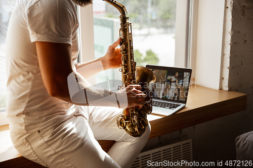 Image of Caucasian musician playing saxophone during concert at home isolated and quarantined, impressive improvising with band connected online
