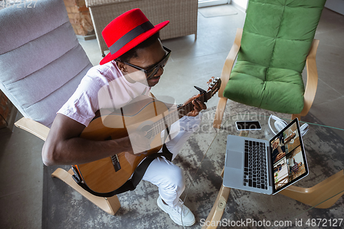 Image of African-american musician playing guitar during online concert at home isolated and quarantined, impressive improvising