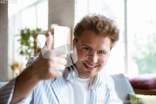 Image of Caucasian musician greeting audience before online concert at home isolated and quarantined, cheerful, smiling