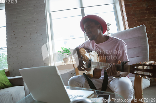 Image of African-american musician playing guitar during online concert at home isolated and quarantined, impressive improvising