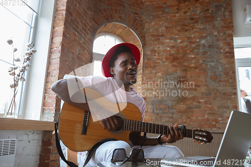 Image of African-american musician playing guitar during online concert at home isolated and quarantined, impressive improvising