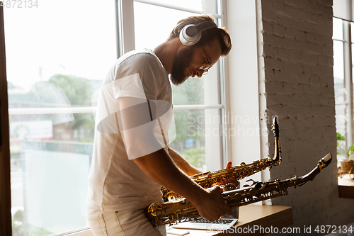 Image of Caucasian musician choosing instrument for concert at home isolated and quarantined, impressive improvising with band connected online