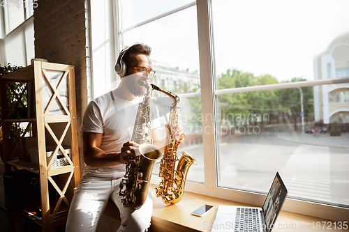 Image of Caucasian musician playing saxophone during concert at home isolated and quarantined, impressive improvising with band connected online