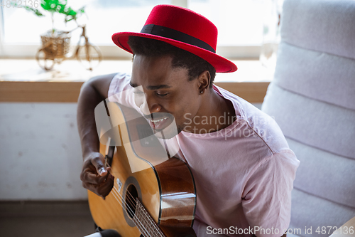 Image of African-american musician playing guitar during online concert at home isolated and quarantined, impressive improvising