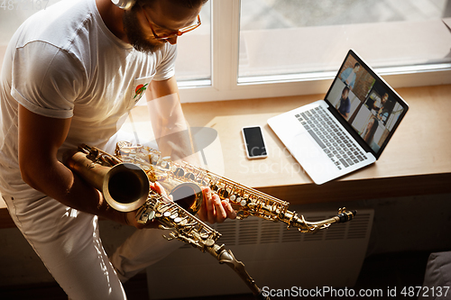 Image of Caucasian musician playing saxophone during concert at home isolated and quarantined, impressive improvising with band connected online