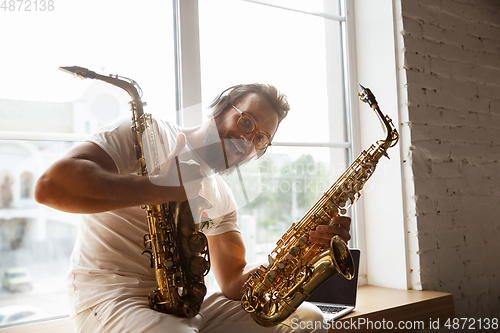 Image of Caucasian musician choosing instrument for concert at home isolated and quarantined, impressive improvising with band connected online