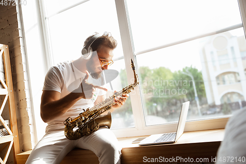 Image of Caucasian musician playing saxophone during online concert at home isolated and quarantined, impressive improvising