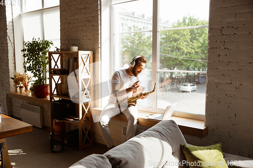 Image of Caucasian musician playing saxophone during online concert at home isolated and quarantined, impressive improvising