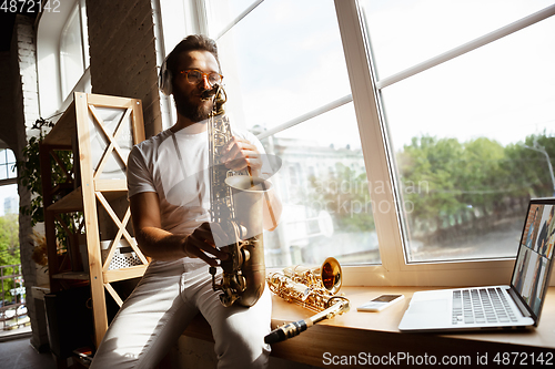 Image of Caucasian musician playing saxophone during concert at home isolated and quarantined, impressive improvising with band connected online