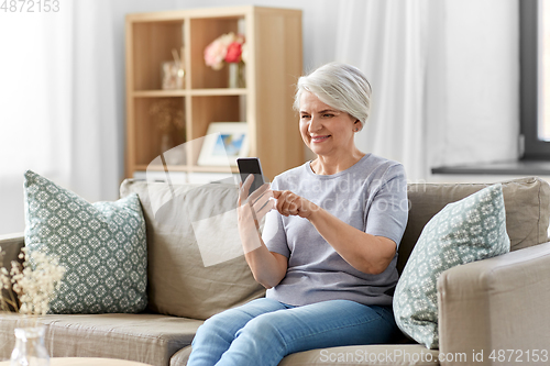 Image of happy senior woman with smartphone at home