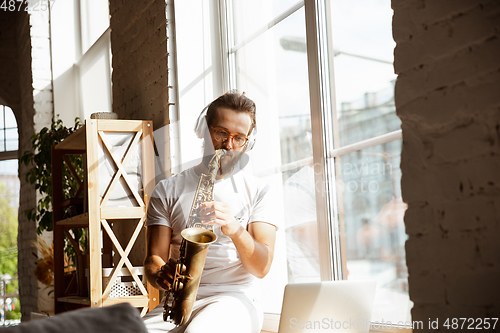 Image of Caucasian musician playing saxophone during online concert at home isolated and quarantined, impressive improvising