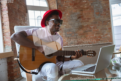Image of African-american musician playing guitar during online concert at home isolated and quarantined, impressive improvising