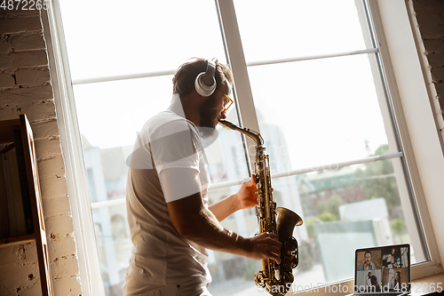 Image of Caucasian musician playing saxophone during online concert at home isolated and quarantined, impressive improvising