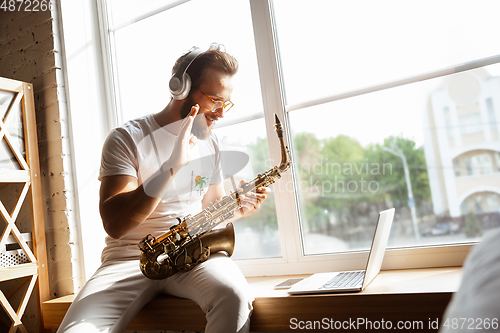 Image of Caucasian musician playing saxophone during online concert at home isolated and quarantined, impressive improvising