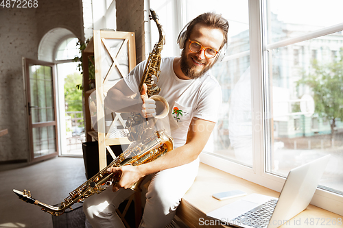 Image of Caucasian musician choosing instrument for concert at home isolated and quarantined, impressive improvising with band connected online