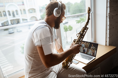 Image of Caucasian musician playing saxophone during online concert at home isolated and quarantined, impressive improvising