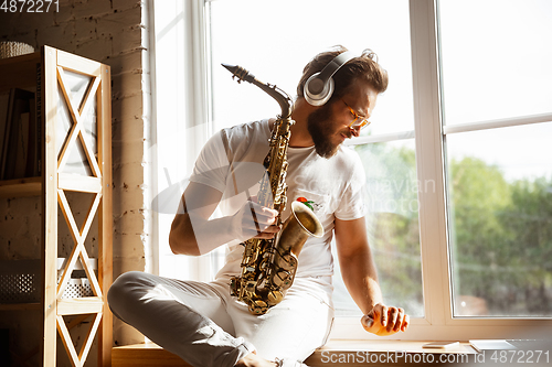 Image of Caucasian musician playing saxophone during online concert at home isolated and quarantined, impressive improvising