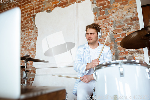 Image of Caucasian musician playing drumms during online concert with the band at home isolated and attented, smiling, cheerful