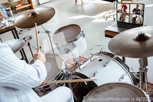 Image of Close up of caucasian musician playing drumms during online concert with the band at home isolated and attented, smiling, cheerful