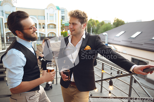 Image of Two men talking, celebrating, look happy, have corporate party at office or bar