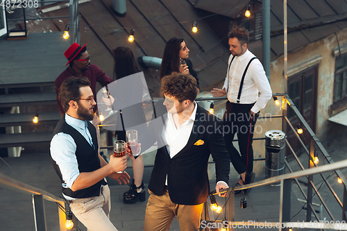 Image of Corporate celebrating in the warm light of the lamps in summer evening, young friends, colleagues look happy, talk, have fun