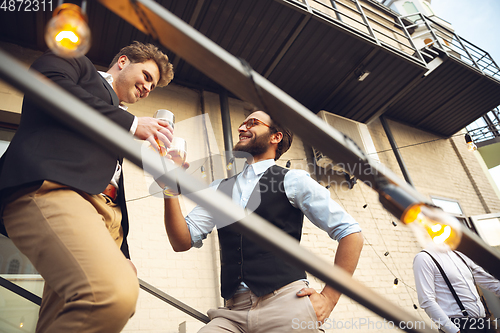 Image of Two men talking, celebrating, look happy, have corporate party at office or bar