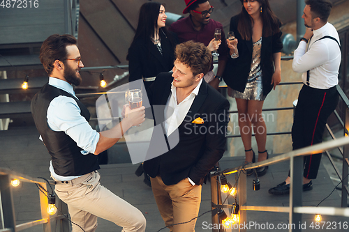 Image of Corporate celebrating in the warm light of the lamps in summer evening, young friends, colleagues look happy, talk, have fun