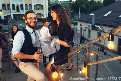 Image of Corporate celebrating in the warm light of the lamps in summer evening, young friends, colleagues look happy, talk, have fun