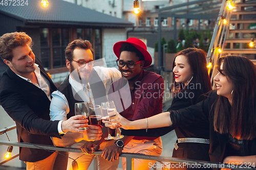 Image of Corporate celebrating in the warm light of the lamps in summer evening, young friends, colleagues look happy, talk, have fun, cheers