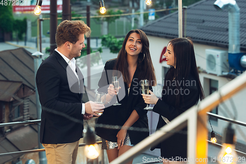Image of Corporate celebrating in the warm light of the lamps in summer evening, young friends, colleagues look happy, talk, have fun