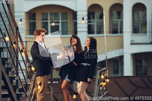 Image of Corporate celebrating in the warm light of the lamps in summer evening, young friends, colleagues look happy, talk, have fun