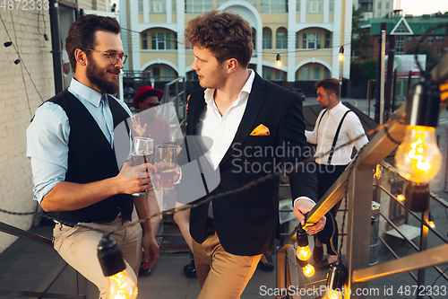 Image of Corporate celebrating in the warm light of the lamps in summer evening, young friends, colleagues look happy, talk, have fun