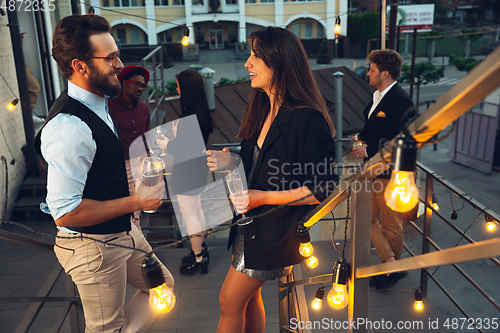 Image of Corporate celebrating in the warm light of the lamps in summer evening, young friends, colleagues look happy, talk, have fun