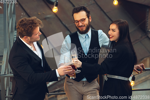 Image of Corporate celebrating in the warm light of the lamps in summer evening, young friends, colleagues look happy, talk, have fun