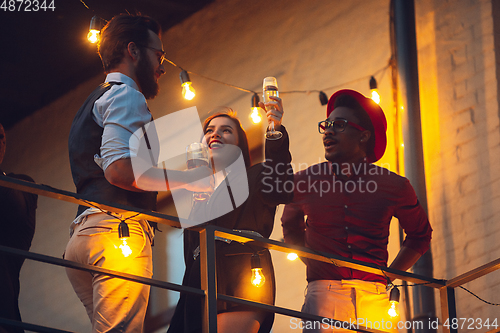 Image of Corporate celebrating in the warm light of the lamps in summer evening, young friends, colleagues look happy, talk, have fun