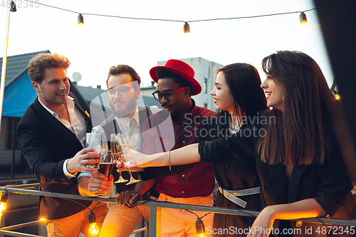 Image of Corporate celebrating in the warm light of the lamps in summer evening, young friends, colleagues look happy, talk, have fun, cheers