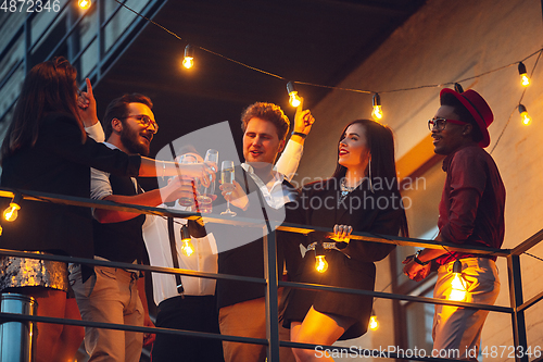 Image of Corporate celebrating in the warm light of the lamps in summer evening, young friends, colleagues look happy, talk, have fun, cheers