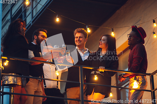 Image of Corporate celebrating in the warm light of the lamps in summer evening, young friends, colleagues look happy, talk, have fun, cheers